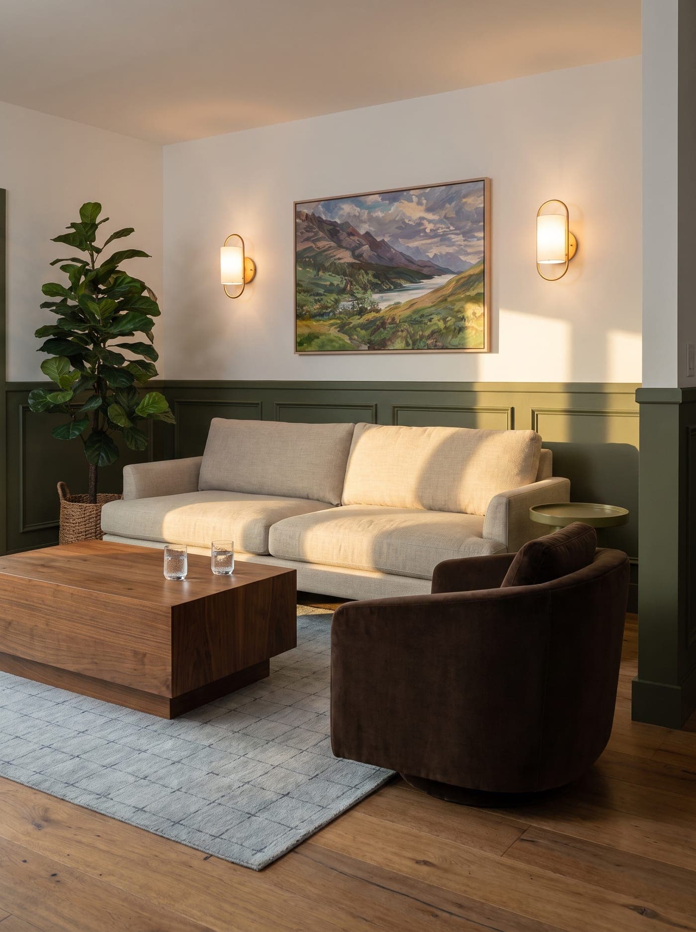 A sofa, a walnut coffee table and a velvet armchair in a sunlit room with olive-green paneling.